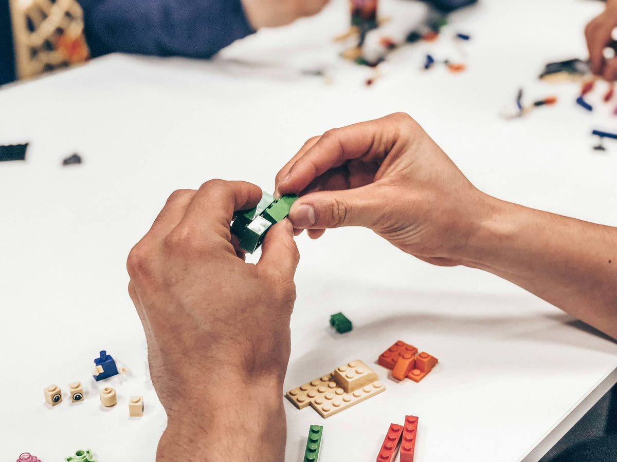 Hands building a LEGO model on a white table